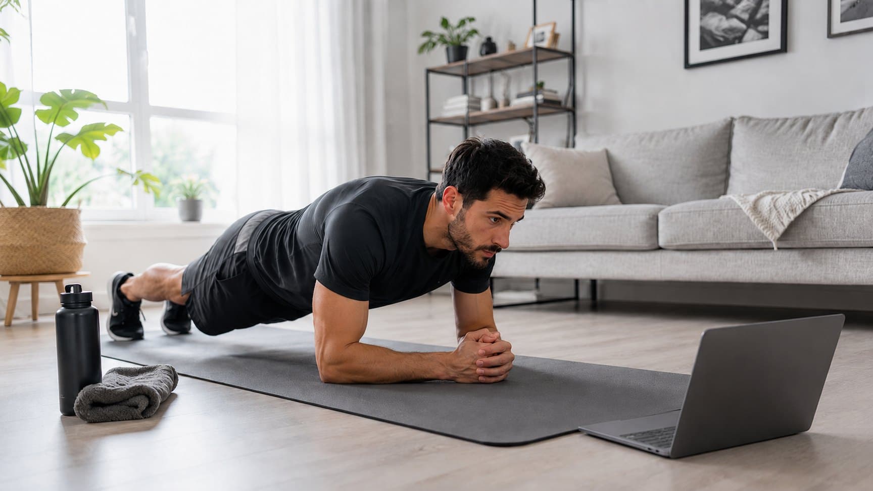 A client holding a plank on a mat at home, following a coached session on a laptop.